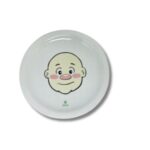 Prato de cerâmica branco, quadrado, com um desenho de um rosto de menina sorrindo, decorado com brócolis como cabelo e outros alimentos para formar um rosto divertido.