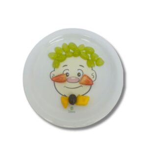 Prato de cerâmica branco, quadrado, com um desenho de um rosto de menino sorrindo, decorado com brócolis como cabelo e outros alimentos para formar um rosto divertido.