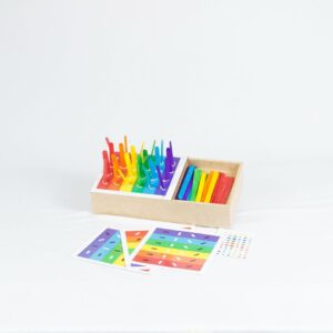 Kit Caixa de Palitos Coloridos da Materiais Para Brincar, mostrando uma caixa de MDF com alguns palitos já inseridos nos orifícios. Uma cartela com um desafio de cores está visível ao lado.