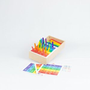 Kit Caixa de Palitos Coloridos da Materiais Para Brincar, mostrando uma caixa de MDF com alguns palitos já inseridos nos orifícios. Uma cartela com um desafio de cores está visível ao lado.