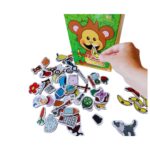 Jogo Fala Certo da Materiais Para Brincar, mostrando uma caixa de madeira com um macaco desenhado. Uma mão de criança está pegando uma ficha magnética da caixa, e bananas estão dispostas ao lado para mostrar a mecânica do jogo.