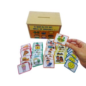 O jogo O que eu fiz no final de semana? da Materiais Para Brincar, mostrando uma caixa de madeira aberta com as fichas de MDF dentro. Algumas fichas estão dispostas em uma mesa ao lado, com as categorias "o que eu comi", "como me senti" e "aonde eu fui?".