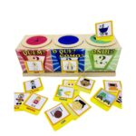 O jogo Quem, O Que e Onde? da Materiais Para Brincar, mostrando a caixa de madeira com os três furos. Algumas figuras (uma pessoa, uma ação, um lugar e um sentimento) estão espalhadas na mesa.
